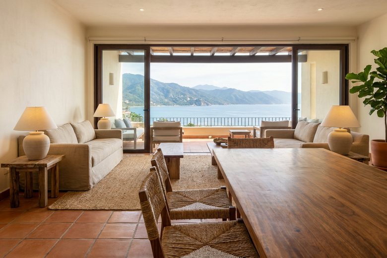Freshly furnished Puerto Vallarta condo living room with a parota wood dining table, neutral sofa, and terrace view of Banderas Bay