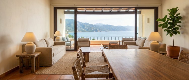 Freshly furnished Puerto Vallarta condo living room with a parota wood dining table, neutral sofa, and terrace view of Banderas Bay