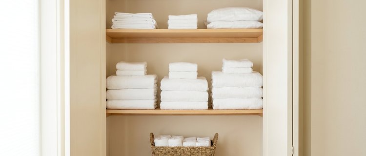 Stacked white linens and folded towels in a vacation rental closet, organized at three sets per bed